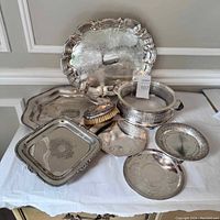Various vintage silver plate serving trays arranged on a white cloth showing shape, patina, and engraving details