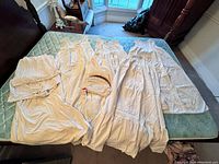 Six white cotton peasant-style dresses laid out on mattress, showing lightweight, gathered fabric and long flowing silhouettes.
