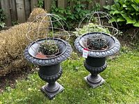 Front angled view of two cast iron urn planters each topped with a wire orb cage