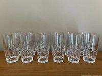 Front view showing 12 clear crystal tumbler glasses arranged in a row highlighting uniform height and clear faceted design.