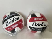 Two Baden youth-sized indoor volleyballs wrapped in plastic packaging. Balls are white, red, and black, labeled 'light' and 'official youth ball'.
