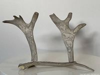 Front view of two carved antler-like pieces with Inuit faces and animal carvings, arranged upright.