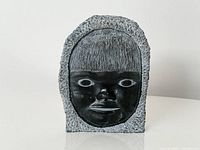 Front view showing one carved Inuit face with polished features and rough textured surround
