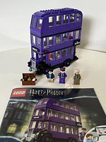 Photo of built purple triple-decker Knight Bus with three minifigures and instruction manual laid out on table.
