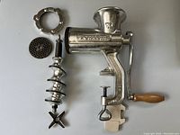 Full view of Porkert #10 cast iron hand crank meat grinder disassembled to show various parts such as the body, screw shaft, cutting blade, and grinder plate.