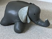 Full side view of dark brown leather elephant ottoman with raised trunk and visible light gray suede inner ears.