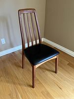 Chair angled view showing teak wood frame and black leather seat on hardwood floor.