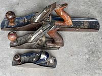 Three hand planes arranged on concrete floor: a long jointer plane at back, a medium bench plane in middle, and a small block plane in front.