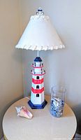 Lighthouse lamp on table showing full height and side angle, with seashell and glass vase with shells as props.
