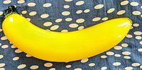 Yellow Murano blown glass banana with green stem tip on a polka dot fabric background shown in profile showing curved banana shape and glass glossiness.