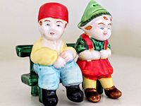 Close-up front angle showing the Dutch boy and girl salt and pepper shakers seated on the green bench.
