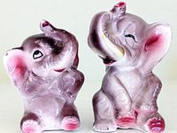 Front and side view of the two pink/purple ceramic elephant salt and pepper shakers with raised trunks and pink accents.