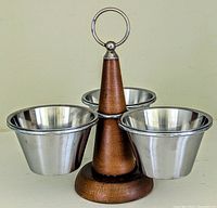 Front view of the vintage mid-century condiment server showing three stainless steel cups mounted on a wooden swivel base with a handle ring on top.