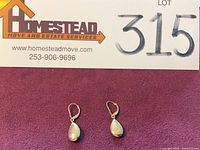 Full view photo showing the pair of 14K gold teardrop dangle earrings on a red background with auction lot card visible.