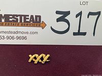 Front view of gold triple X pin on burgundy background with partial lot card