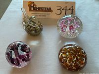 Four art glass paperweights arranged on a white surface with a lot sign visible