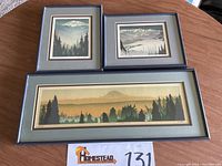 Three framed watercolor prints on round wooden table in blue-gray triple mats
