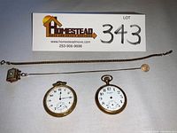 Two pocket watches, one with an ornate gold tone case and one with an engraved elk motif case, alongside two chains with fobs.