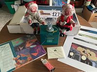 Two vintage sitting Scandinavian elves seated on a surface with the Disney Enchanted Places Cinderella's Castle ornament and box, several Disney prints, and vintage bendable Santa figure in front.