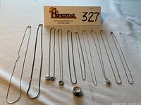 Overview of all 8 silver necklaces/chains and one ring laid out on a white surface, showing variety of chain types and pendant details.