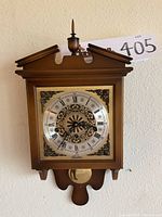 Full view of the wooden wall clock showing dial, pendulum and decorative finial top.