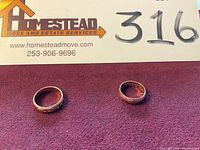 Two gold bands side by side on red cloth with Homestead move and estate services card and lot number marker