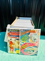 Front view of Shazam #20 and Aquaman #40 issues standing in front of full comic box