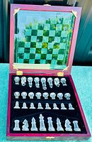 Opened wooden box showing all 32 frosted and clear glass chess pieces arranged in velvet compartments with the glass chessboard inside the lid.