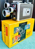 Front and side view of Kodak Brownie Movie Camera showing three lenses and original yellow box with colorful usage photos.