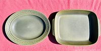 Top view of both serving dishes showing one oval with textured rim and one square with handles, green glaze in sunlight