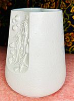 Front view of white porcelain vase showing matte textured surface and inset side with detailed marine life relief including seahorse and various shells.