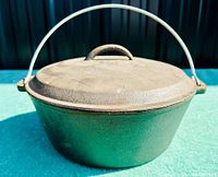 Front view of vintage cast iron Dutch oven with lid and metal bail handle showing overall shape and condition.