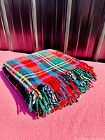 Folded vintage wool plaid tartan blanket with visible multicolor fringe detail.