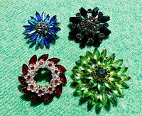 Top-down view of all four vintage rhinestone brooches arranged in a square formation on a green textured background