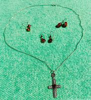 Full view of sterling silver necklace with Baltic amber crucifix pendant and three pairs of amber and silver earrings laid out on green fabric.