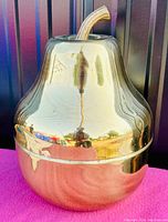 Side view of pear shaped solid brass ice bucket with shiny surface on pink cloth background.