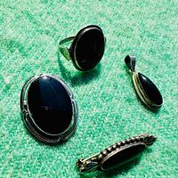 Four pieces of vintage sterling silver jewelry with black onyx stones displayed on green felt background, showing brooch, ring, and two pendants