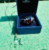 Photo showing large purple Swarovski crystal ring inside the blue Swarovski box and clear crystal snowflake pendant necklace on brown cord lying on green surface.
