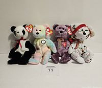 Four Ty Beanie Baby teddy bears standing in a row on a white background, displaying front sides with tags visible.