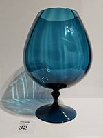 Front view of teal Empoli art glass brandy snifter showing rounded bowl with scalloped rim and flared pedestal base, on white background with lot number identifer.