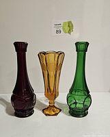 Three coin glass vases in red, amber, and green on a white surface shown from front.