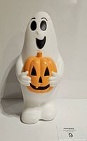 Front view of white ghost blow mold holding orange Jack O Lantern pumpkin with smiling face and black eyes.