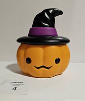 Front view of the unlit pumpkin blow mold showing the orange pumpkin with black eyes and mustache-like mouth topped with a black witch hat with purple band.