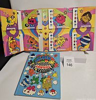 Photo of eight Mr Men and Little Miss thick paperback books arranged open to show back covers with colorful character art and matching envelopes below. Mr Men Annual laid beside them with a sky blue cover featuring Mr Men characters in a hot air balloon.