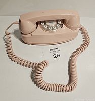 Front view of retro pink Crosley telephone on white surface showing handset placed on cradle, coiled cord extended.