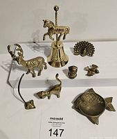 Overview of most brass items on white background showing bell with carousel horse, deer, cat, peacock, bust, fish dish and others.
