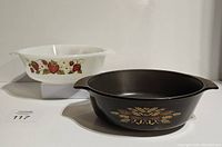 Two vintage baking dishes shown side by side: a white milk glass strawberry motif dish and a brown Teflon-coated Anchor Hocking dish