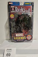 Front view of packaged Marvel Legends Red Skull action figure with stone wall background and turret accessory visible.