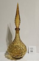 Amber bubble glass Empoli squat genie bottle with stopper, displayed against a white background with a lot number card visible. Shows side profile highlighting bubble texture and shape.