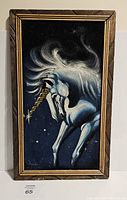 Front view of black velvet painting showing a white unicorn with golden horn and flowing mane in wooden frame.